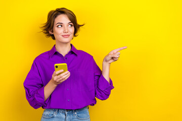 Photo of charming person hold smart phone look direct finger empty space wear violet isolated on yellow color background