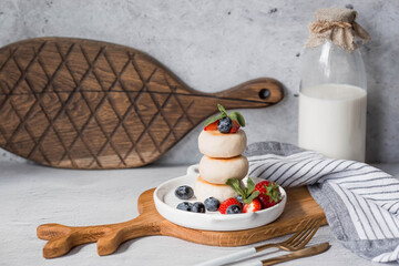 Cottage cheese pancakes, Russian cheesecakes with fresh blueberries, strawberries and mint on a stylish wooden board on a gray concrete table. Natural products. Healthy and delicious breakfast.