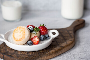 Cottage cheese pancakes, Russian cheesecakes with fresh blueberries, strawberries and mint on a stylish wooden board on a gray concrete table. Natural products. Healthy and delicious breakfast.