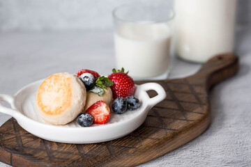 Cottage cheese pancakes, Russian cheesecakes with fresh blueberries, strawberries and mint on a stylish wooden board on a gray concrete table. Natural products. Healthy and delicious breakfast.