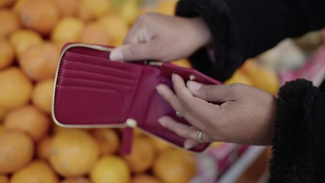 Young african american woman showing empty wallet at fruit store