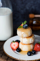 Cottage cheese pancakes, cheesecakes with fresh blueberries, strawberries, honey and mint leaves on a stylish wooden board on a dark background. Natural products. Healthy and delicious breakfast.