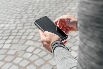A man with a smartphone in his hands sits in the middle of the city in daylight