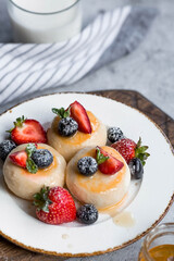 Cottage cheese pancakes, cheesecakes with fresh blueberries, strawberries, honey and mint leaves on a stylish wooden board on a gray concrete table. Natural products. Healthy and delicious breakfast.