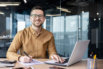 Portrait of young businessman in shirt, man smiling and looking at camera at workplace inside...