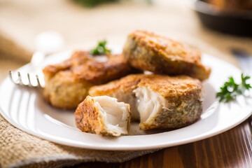 A piece of hake fish fried in a crispy crust, in a plate.