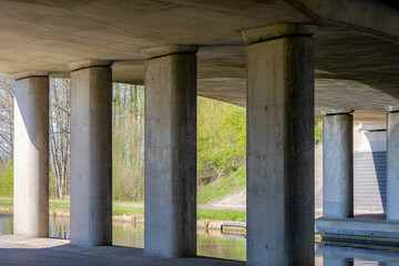 Cement concrete pillar structure of urban bridge crossing over small river, canal or ditch with the shadow, Underneath of classic style bridge with sunlight and green grass on the ground.