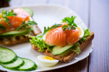 fried toast with lettuce, egg, cucumbers and red fish in a plate.