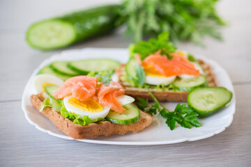 fried toast with lettuce, egg, cucumbers and red fish in a plate.
