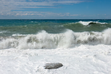 Large waves breaking over a rocky beach. Mediterranean storm on a sunny day