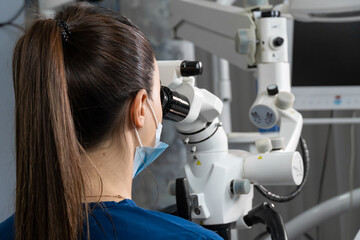 Female dentist using dental microscope treating patient teeth dental clinic office. undergoing treatment by experienced dentist using microscope. Image of woman on patient's chair in dentist's office.