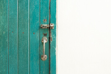 The Closed padlock hangs on the green color wooden door and wall.