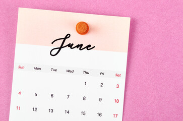 The June 2023 and wooden push pin on pink color background.