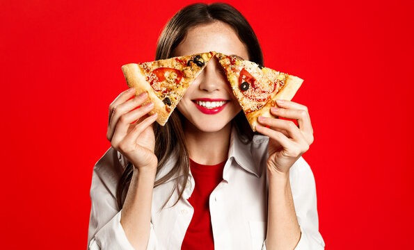 Portrait of young smiling woman, covers her eyes with slices of pizza, orders takeaway from italian restaurant, stands over red background