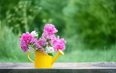 flowers bouquet in yellow watering can on table outdoor, green natural background. floral decor in garden. romantic atmosphere nature image. spring, summer season. template for design. copy space