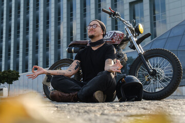 Obraz premium Shot of motorcyclist macho with tattooes relaxing outdoors against background of building.