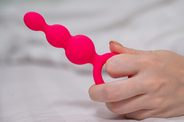 Close-up of a female hand with pink anal beads lying in bed. 