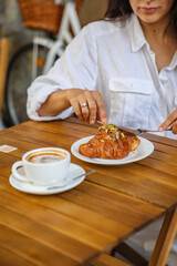 Obraz na płótnie Canvas A woman eats breakfast on the terrace a crispy croissant and a cup of coffee