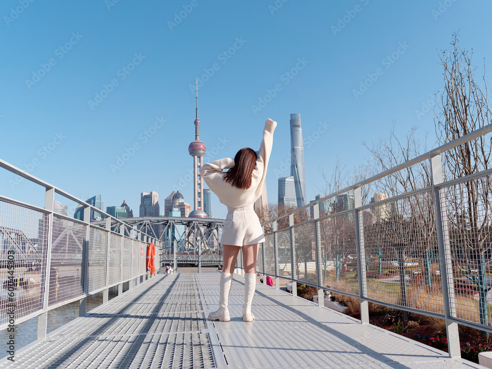 Wall mural Rear view of beautiful young woman with black long hair in white skirt posing with Shanghai city bund landmarks background in sunny day. Emotions, people, beauty, travel and lifestyle concept.