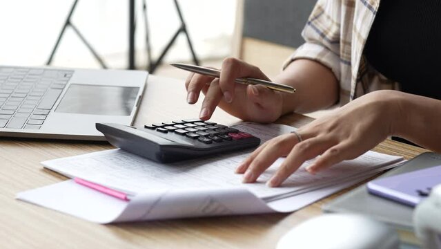 Close up hand of woman using calculator for calculate checking bills, taxes, bank account balance and calculating expenses in the living room at home.