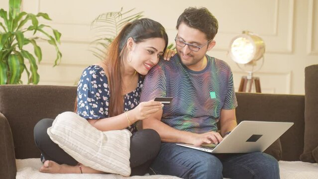 Happy excited indian couple making online payment for shopping using credit card on laptop at home - concept of relationship, e-commerce and secure banking