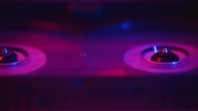 Audio engineer puts a cassette tape into a professional recorder and starts the recording during the studio session in a color light close up