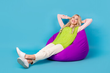 Obraz premium Full size photo of cheerful nice girl sit cozy bag arms behind head enjoy free time isolated on blue color background