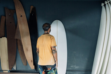 Unrecognizable man examining surfboard in workshop