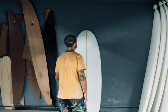 Unrecognizable man examining surfboard in workshop