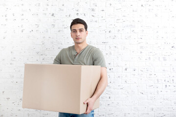 Handsome man carrying heavy box in front of white brick wall background