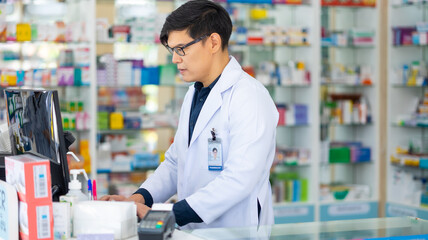 Male working on computer. Pharmacy Drugstore. Portrait Professional Pharmacist handsome asian man at pharma store. Health and wellness center