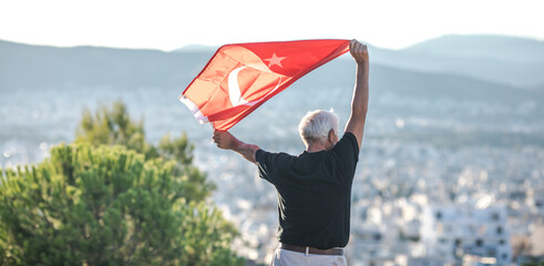Patriotic senior man celebrates Turkish independence day with a national flag in his hands. Constitution and Citizenship Day.