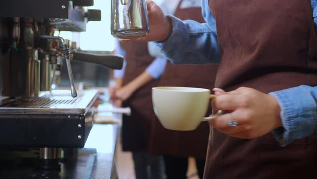 Closeup hands of barista preparing making coffee cappuccino or latte while pouring milk in coffee cup in cafe, close-up young asian woman making beverage on mug in coffeeshop, small business or SME.