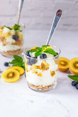 blueberry and golden kiwi yogurt parfait in a glass on white background.
