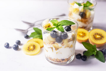 blueberry and golden kiwi yogurt parfait in a glass on white background.