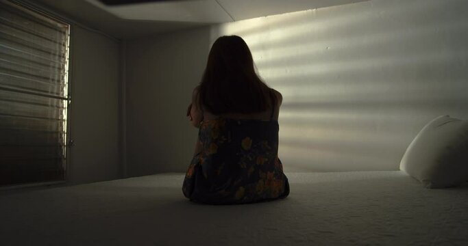 A lonely woman is sitting on the bed in a narrow dark room. This concept use for symptoms of stress, major depressive disorder (MDD), psychotic symptoms.