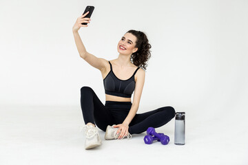 Young fitness trainer instructor woman doing exercises do selfie shot on mobile cell phone sit on mat floor at home gym indoor