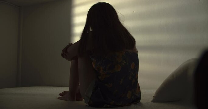 A lonely woman is sitting on the bed in a narrow dark room. This concept use for symptoms of stress, major depressive disorder (MDD), psychotic symptoms.