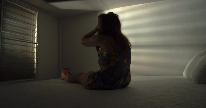 A lonely woman is sitting on the bed in a narrow dark room. This concept use for symptoms of stress, major depressive disorder (MDD), psychotic symptoms.