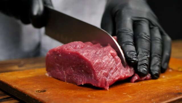 A butcher in gloves cuts a carcass of red meat.Close-up of a professional knife cutting a huge piece of meat in a butcher's shop on a cutting board