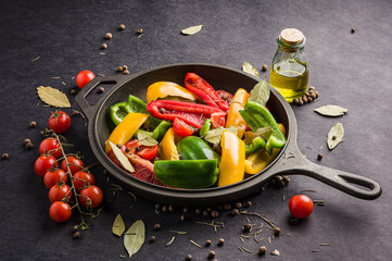 Vegetables, peppers and cherry tomatoes in a black frying pan bay leaf and a small bottle of olive oil on a black background