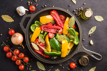Vegetables, peppers and cherry tomatoes in a black frying pan with garlic, onion, bay leaf and a...