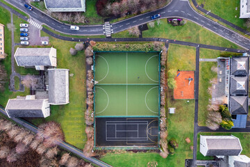 Sport ground in a college or university student camp. Aerial top down view on basketball, tennis and mini soccer or football court and walking path and houses and road.
