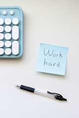 work hard written on a sticky note at desk with keyboard and pen
