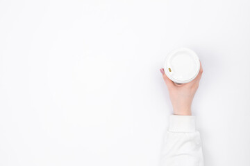Disposable paper cup in a female hand on a white background, top view.