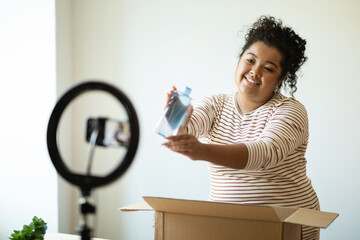 Beauty blogger hispanic woman unpacking parcel at home, recording video
