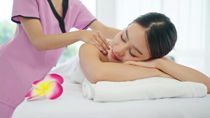 Obraz na płótnie Canvas Happy and relaxed young Asian woman lying on massage bed closed eyes and relaxed while masseuse massaging back and shoulders. Body relaxation concept