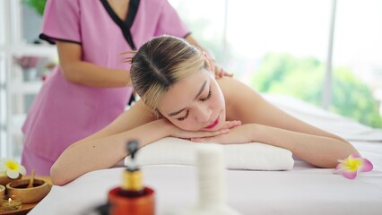 Healthy and beautiful Asian woman lying on massage bed closed eyes relaxing receiving back and shoulders massage. Spa treatment concept
