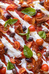 Pizza con pomodori secchi, pomodorini, mozzarella, burrata, basilico e olive, primo piano, inquadratura verticale