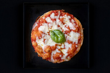 Pizza rotonda con pomodoro, mozzarella e basilico su sfondo nero